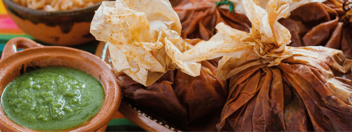 Mixotes de pollo envueltos en hoja de maguey con un plato de salsa verde a un lado